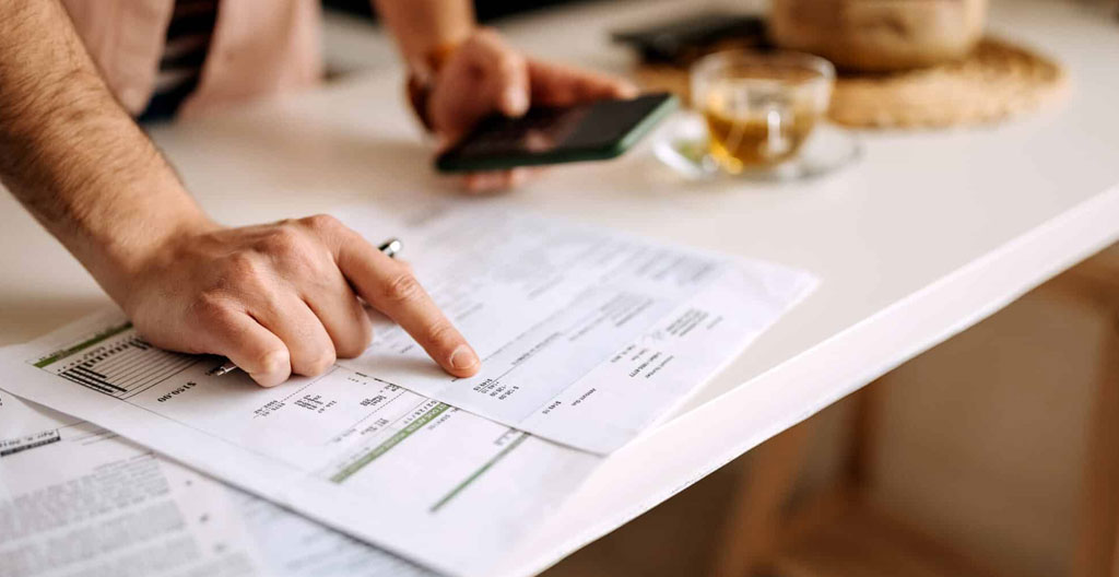 Des mains tiennent une facture papier tandis qu'un stylo pointe une ligne, bureau en arrière-plan avec lumière naturelle